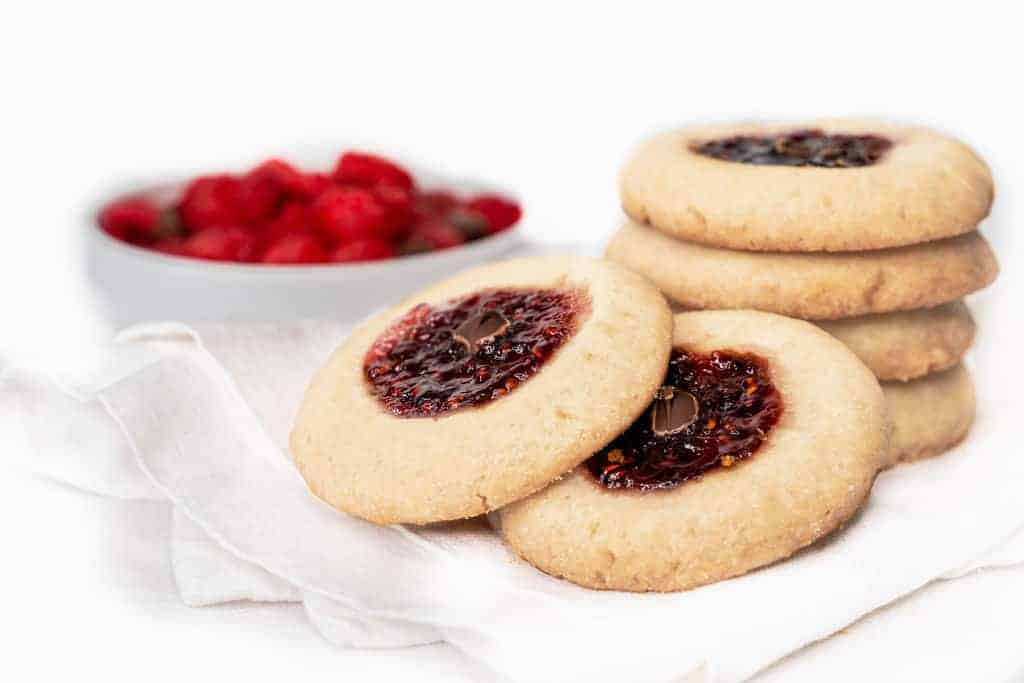 four Raspberry Thumbprint Cookies with raspberries in a white bowl in a white background