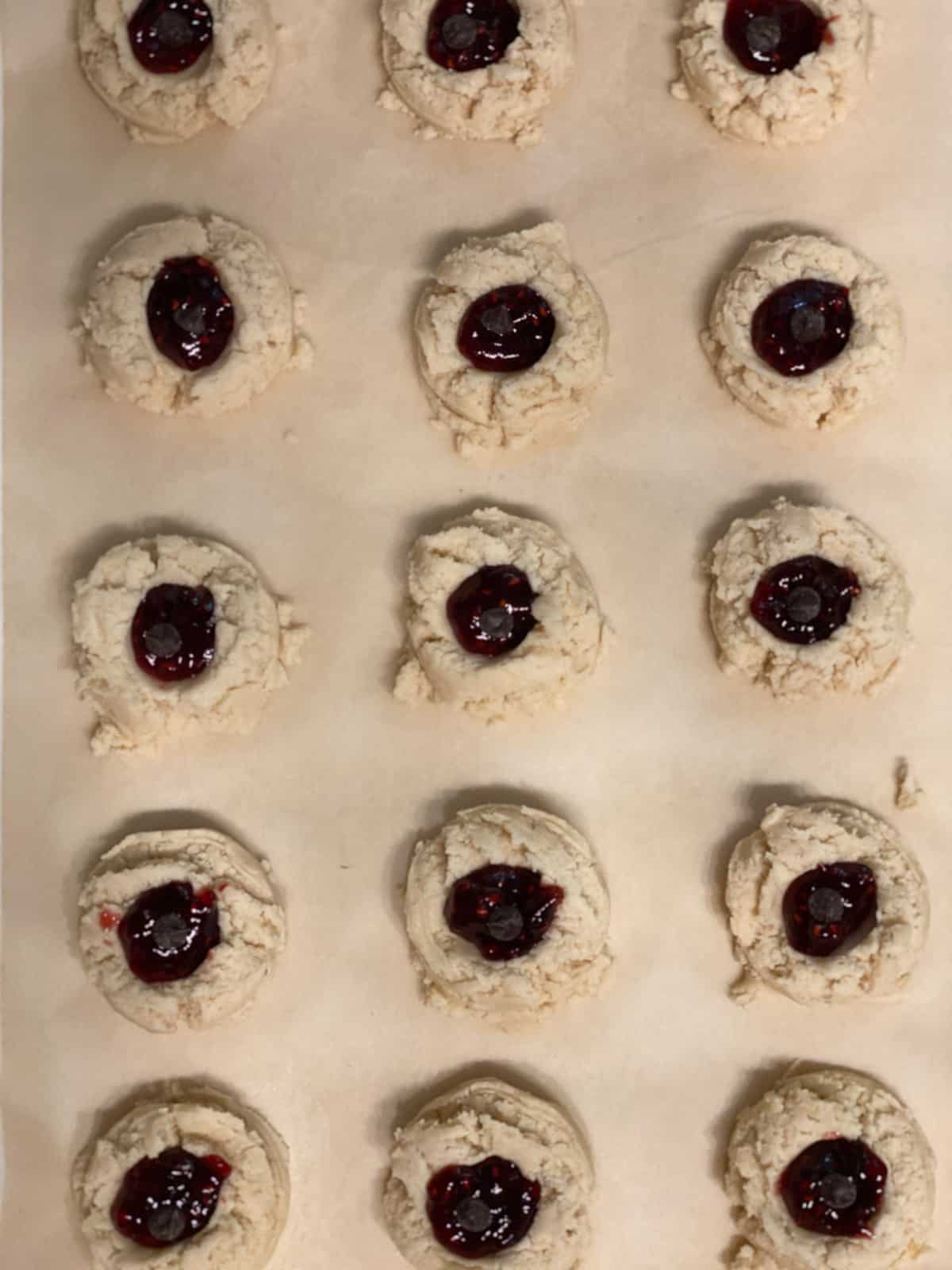 pre baked Raspberry Jam Thumbprint Cookies scattered on a baking sheet