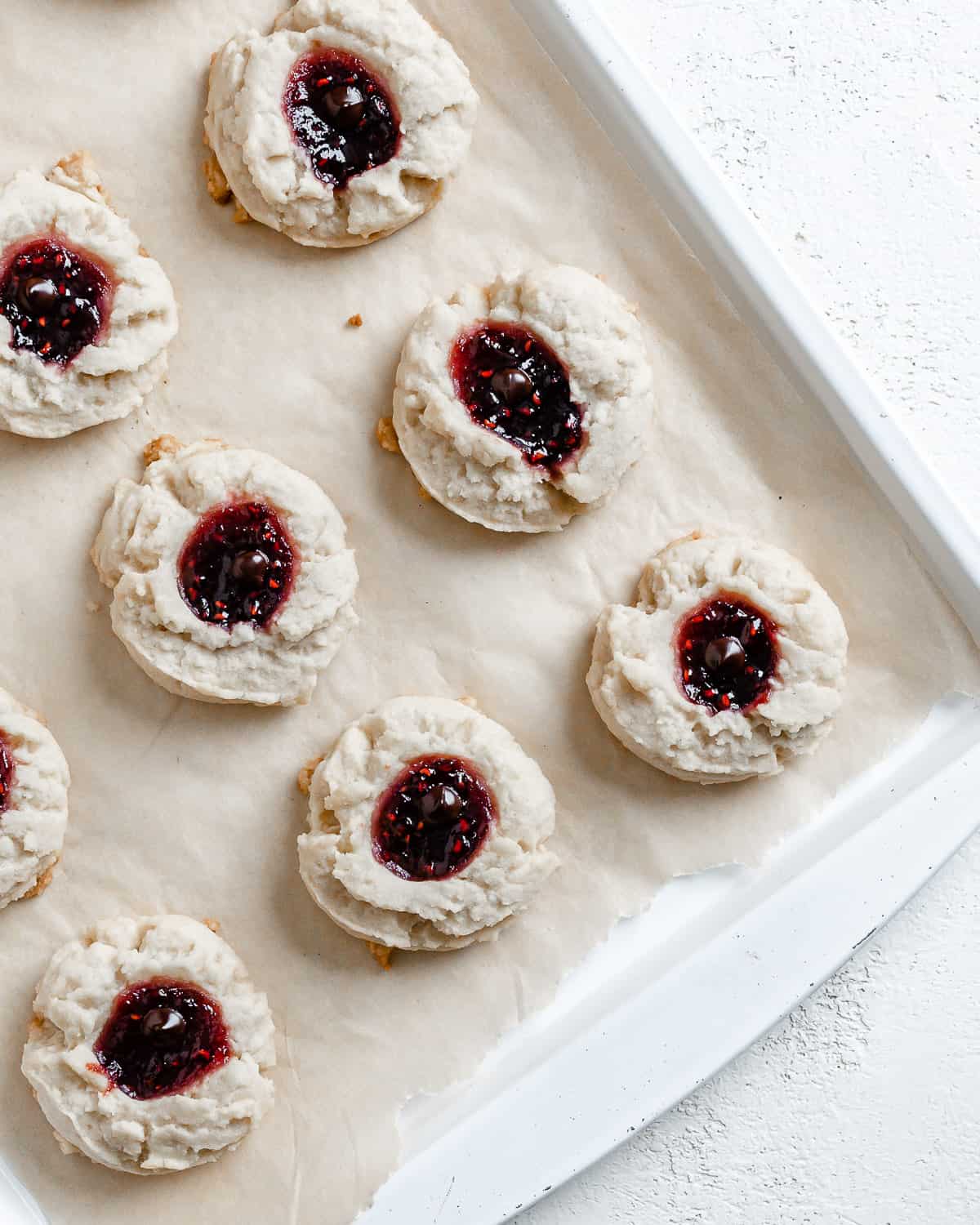 completed Raspberry Jam Thumbprint Cookies scattered on a baking sheet