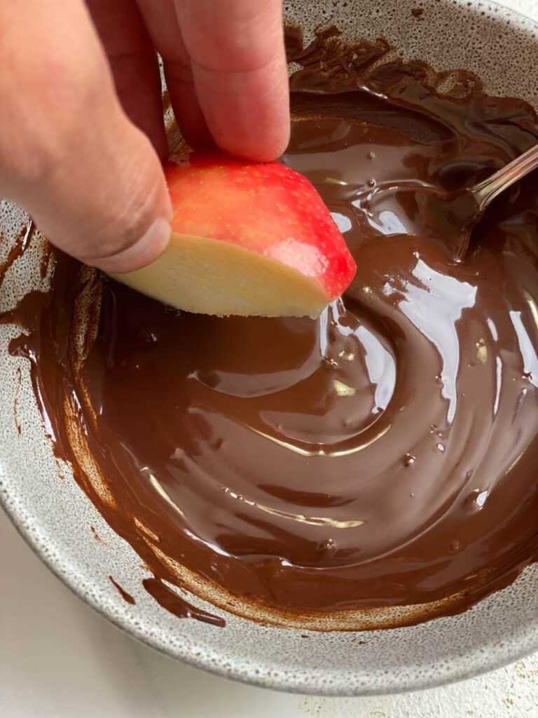 process shot of dipping apples in bowl of melted vegan chocolate