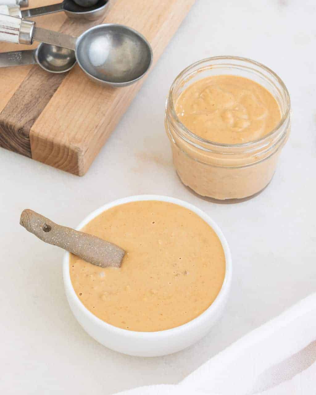completed peanut sauce in a white bowl and small clear jar against light background