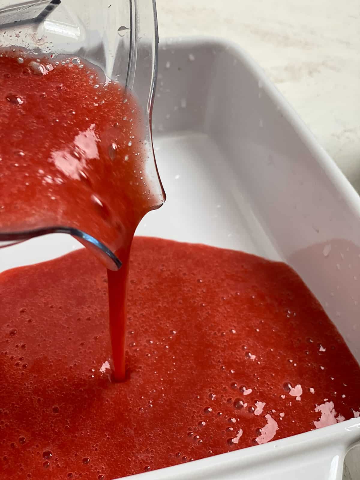 process of pureed strawberry sorbet mixture being poured into white tray