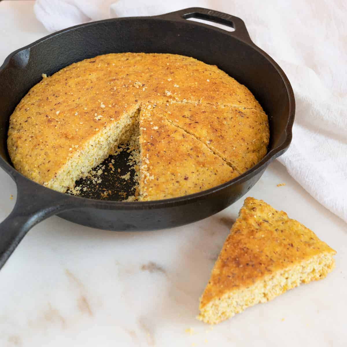 completed cornbread in skillet with one triangular piece on a white surface