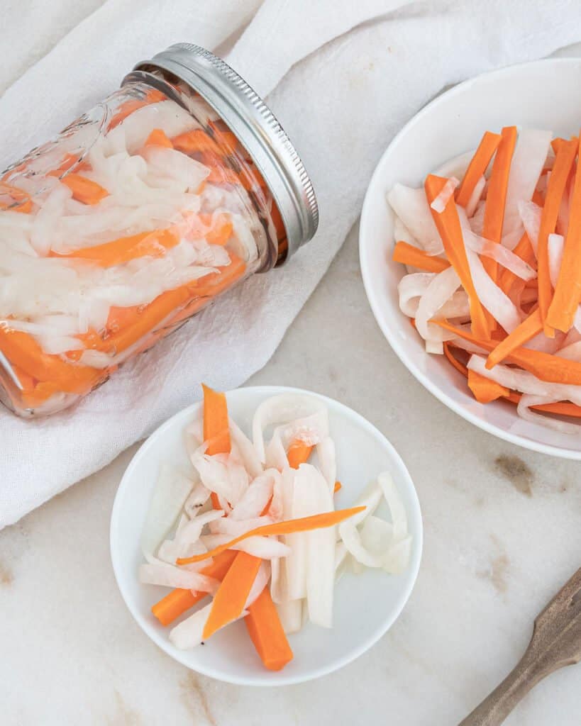 finished pickled carrots in a jar and in two separate bowls against a white background