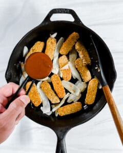 the process of adding BBQ sauce to a pot with tempeh and onion