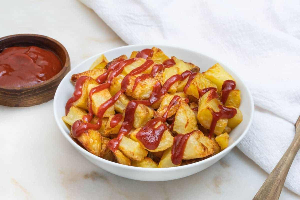 completed patatas bravas in a white plate with sauce on top and on the side