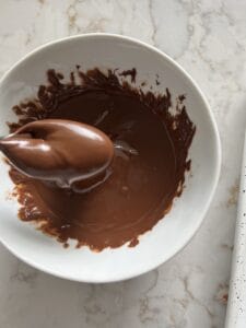 process of melting chocolate in a small white bowl against a white marble surface