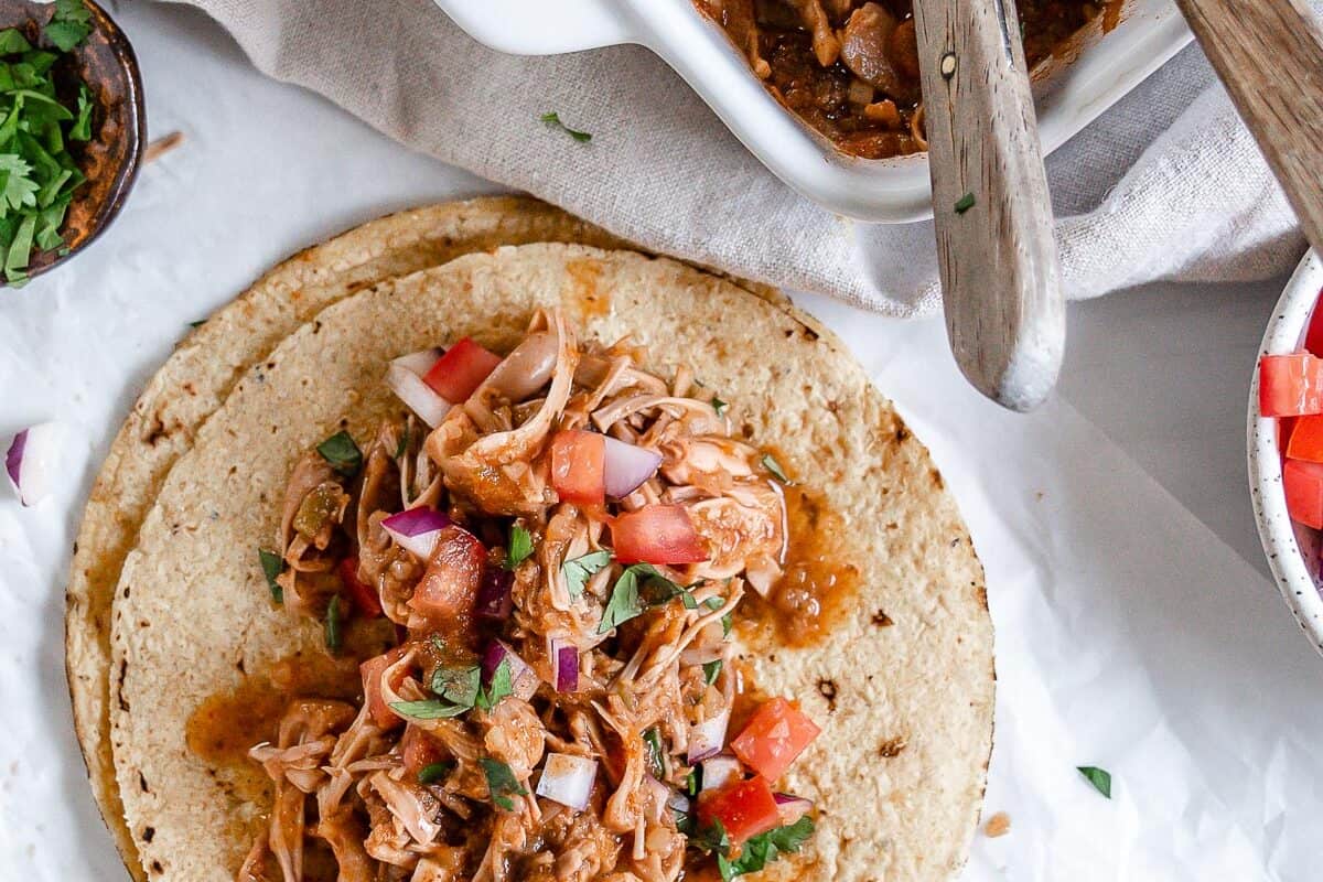 completed jackfruit carnitas on tortillas against a white background with ingredients in the background