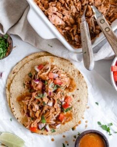 completed jackfruit carnitas on tortillas against a white background with ingredients in the background