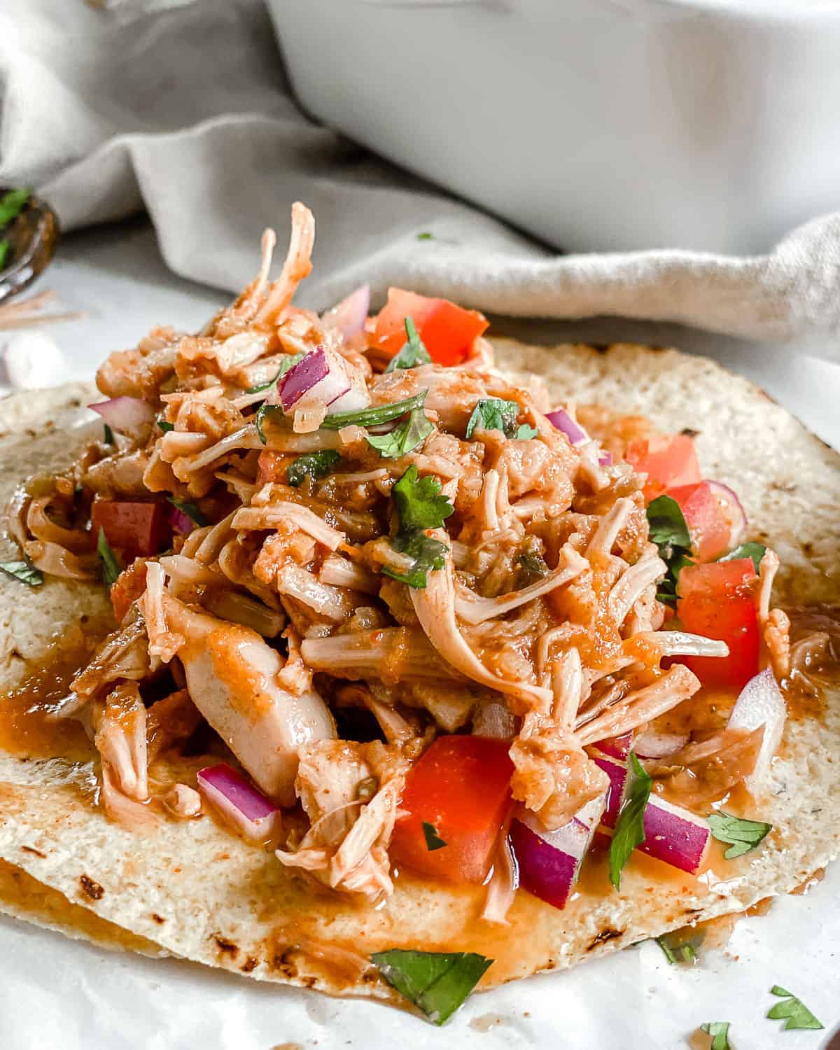 completed jackfruit carnitas on tortillas against a white background with ingredients in the background