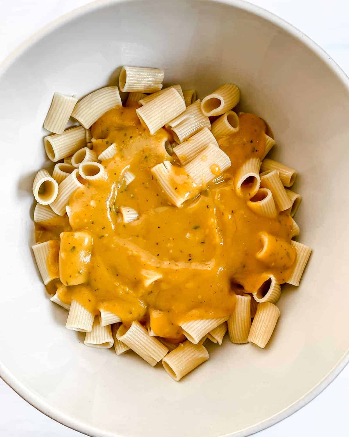 process showing Pumpkin Pasta Bake with ingredients being added to the pasta in a white bowl