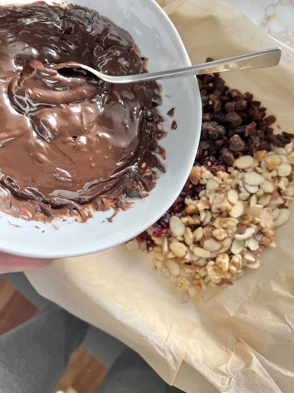 process of adding melted vegan chocolate to fruit and nut mixture