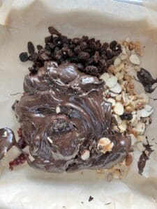 mixture of melted chocolate, dried nuts, and nuts on parchment paper