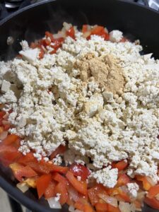 process of adding tofu crumbles into pot with veggies
