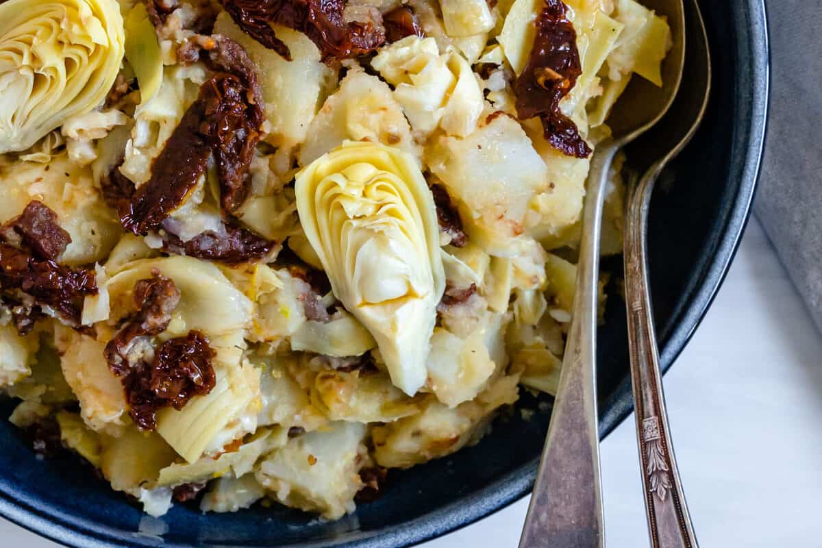 completed Artichoke Potato Salad with Lemon Dressing in a blue bowl with two utensils in the bowl