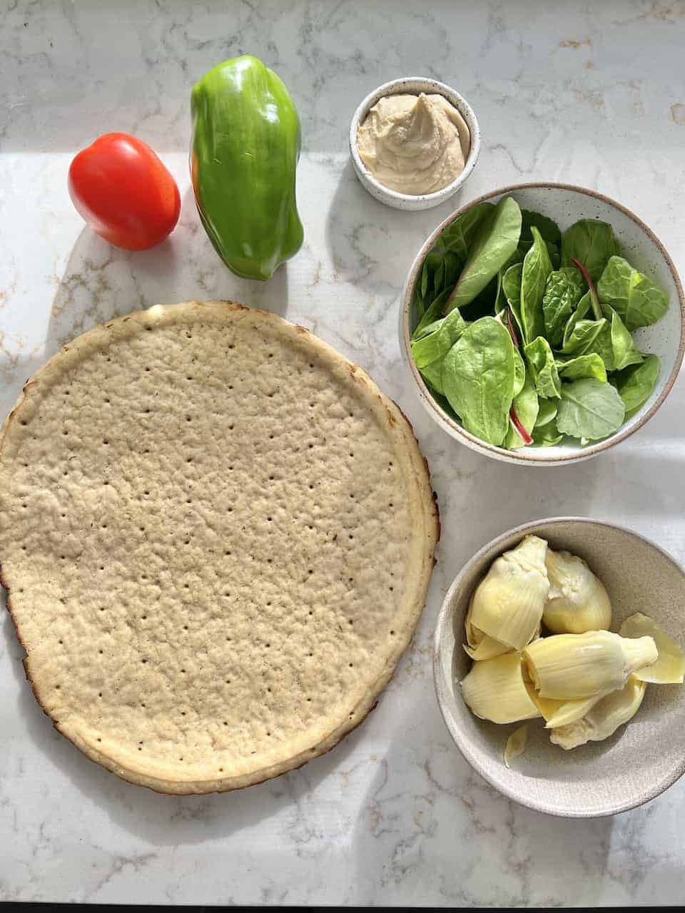 ingredients measured out for hummus pizza on white surface