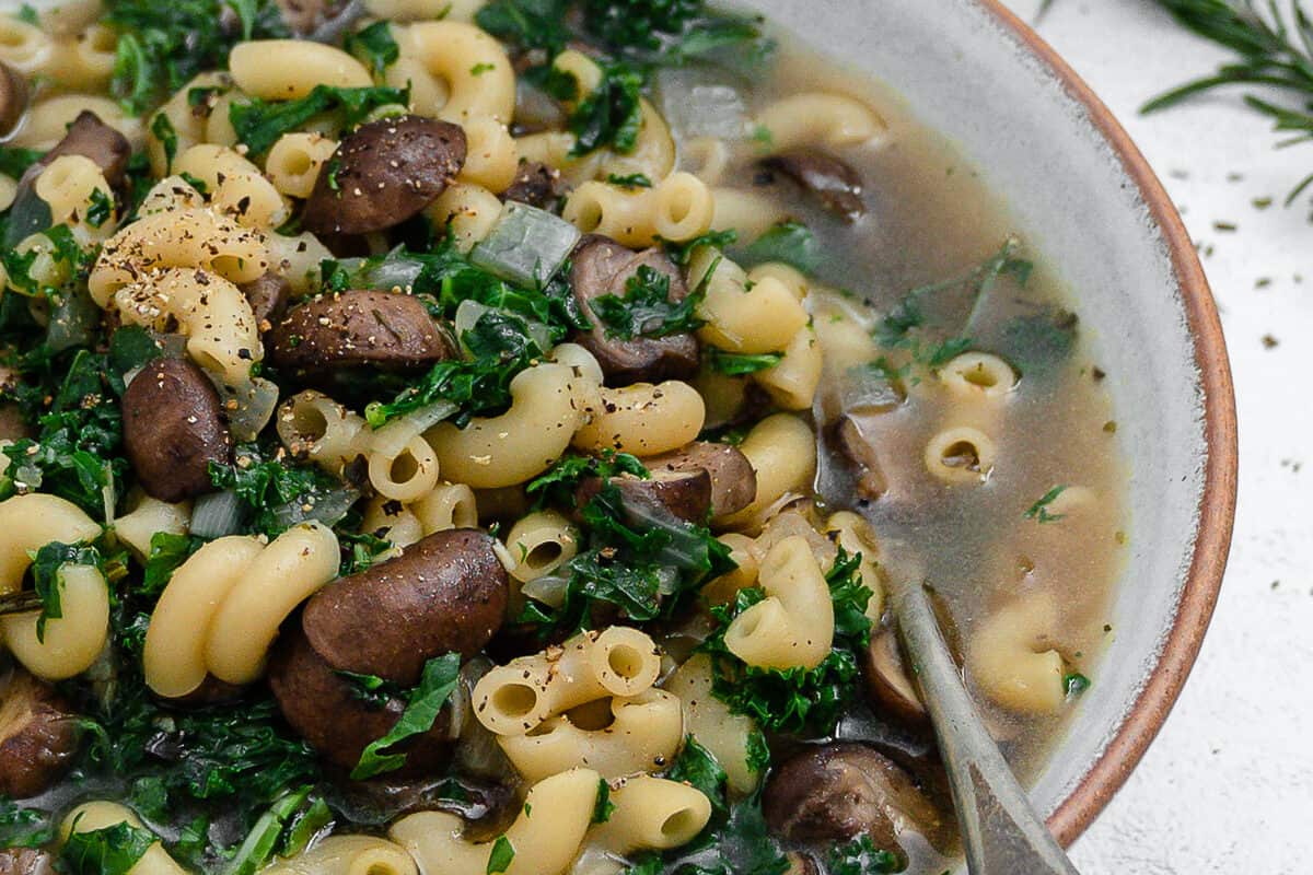 completed mushroom orzo soup in a white bowl with a spoon inside the bowl against a white background