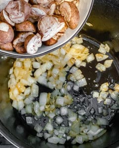 process of mushrooms being poured into black skillet with onion and garlic