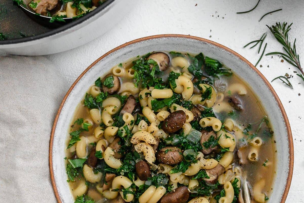completed mushroom orzo soup in a white bowl with a spoon inside the bowl against a white background