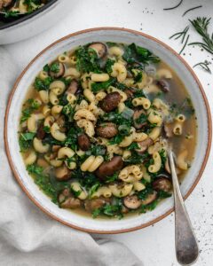 completed mushroom orzo soup in a white bowl with a spoon inside the bowl against a white background
