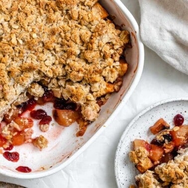 completed Apple Cranberry Crisp with a piece plated on a small white pplate against a white background