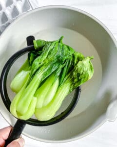 process of baby bok choy being taken out of ice water bowl 