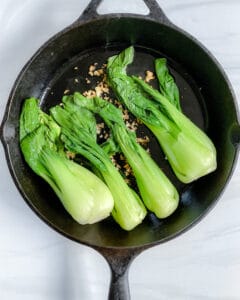process showing baby bok choy being added to skillet with oil and garlic