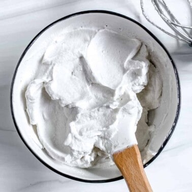 completed vegan whipped cream with mixing utensil in bowl against white background