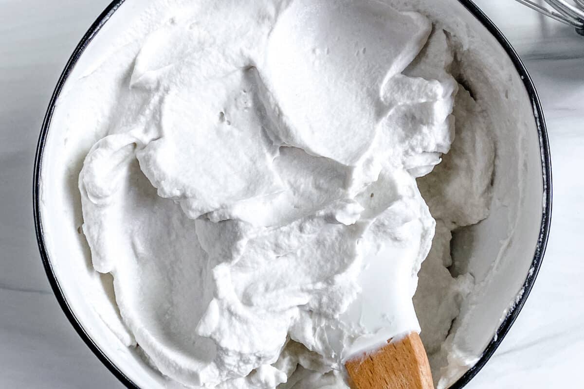 completed vegan whipped cream with mixing utensil in bowl against white background
