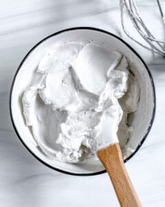 completed vegan whipped cream with mixing utensil in bowl against white background
