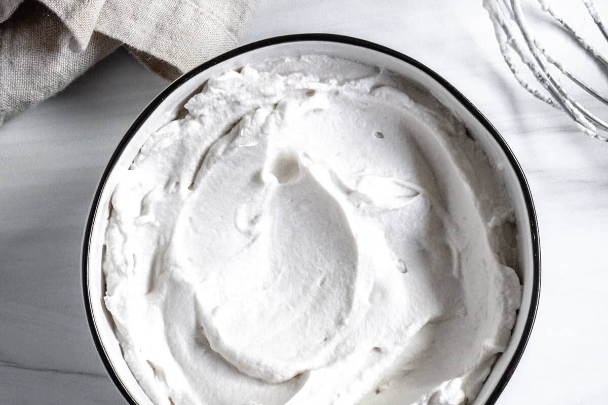 completed vegan whipped cream with mixing bowl against white background
