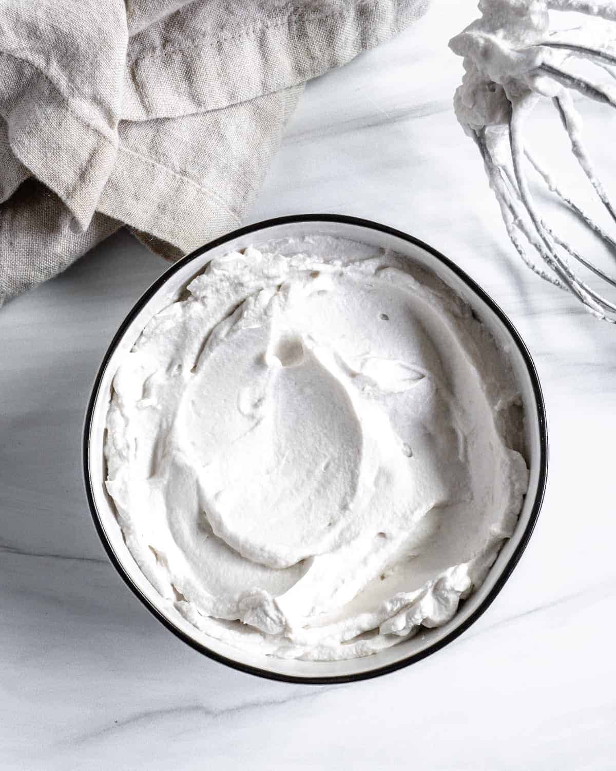 completed vegan whipped cream with mixing bowl against white background