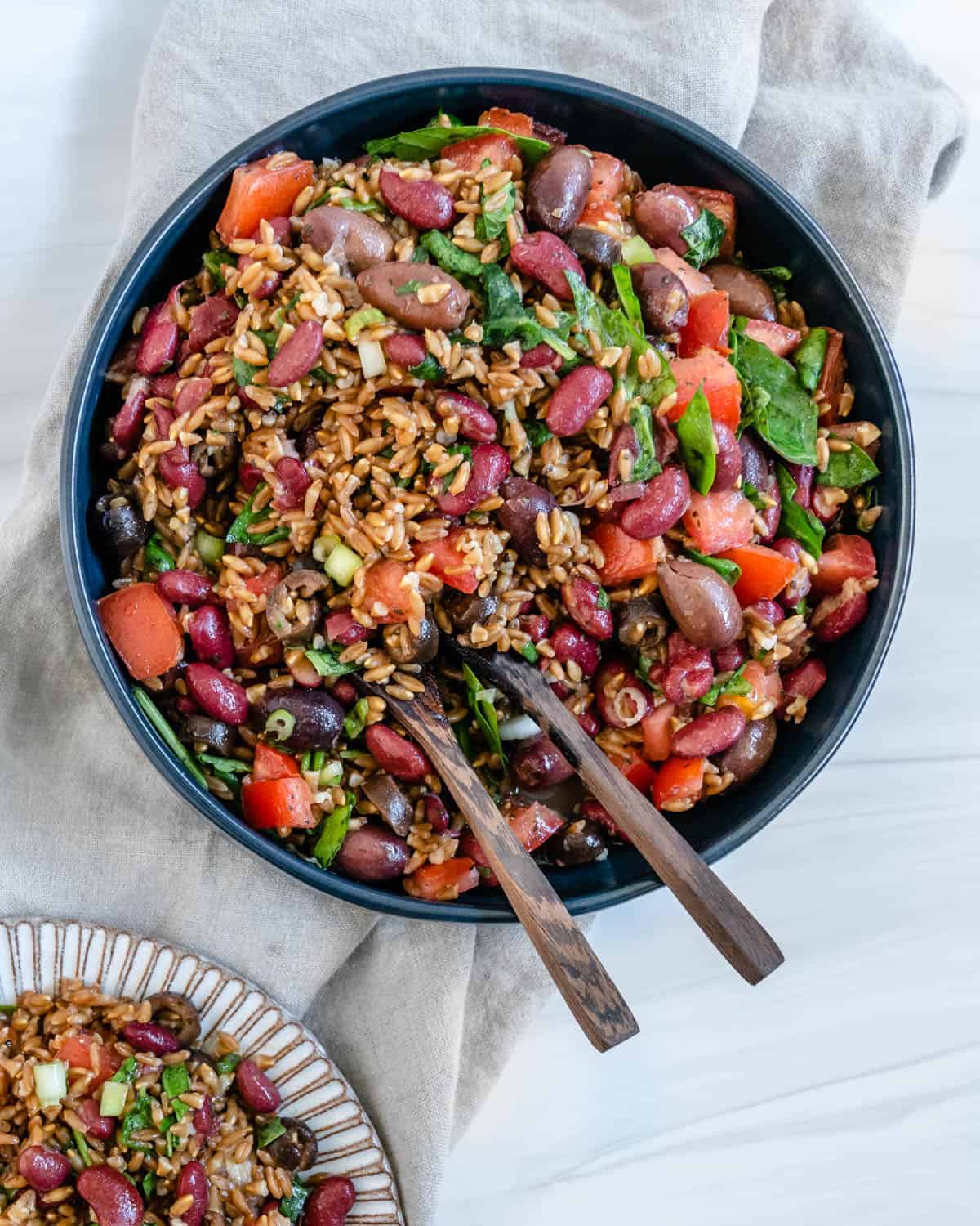 completed Colorful Farro Salad in a blue bowl with utensils in it against a light background