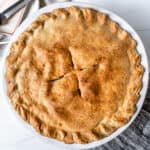 completed apple pie in a white circular pan against a white background
