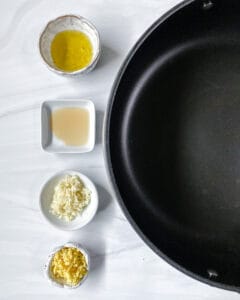 measured out spices and oils next to a black pan against a white background