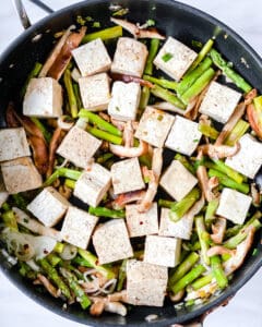 process of cooking Shiitake Asparagus Tofu Stir-fry in a black pan with the addition of tofu