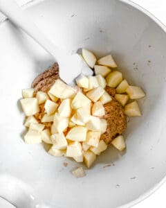 process of mixing in apples to batter in white bowl