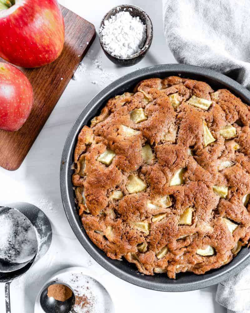 finished apple cake with two apples and measuring tools against a white background