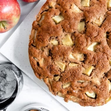 finished apple cake with two apples and measuring tools against a white background