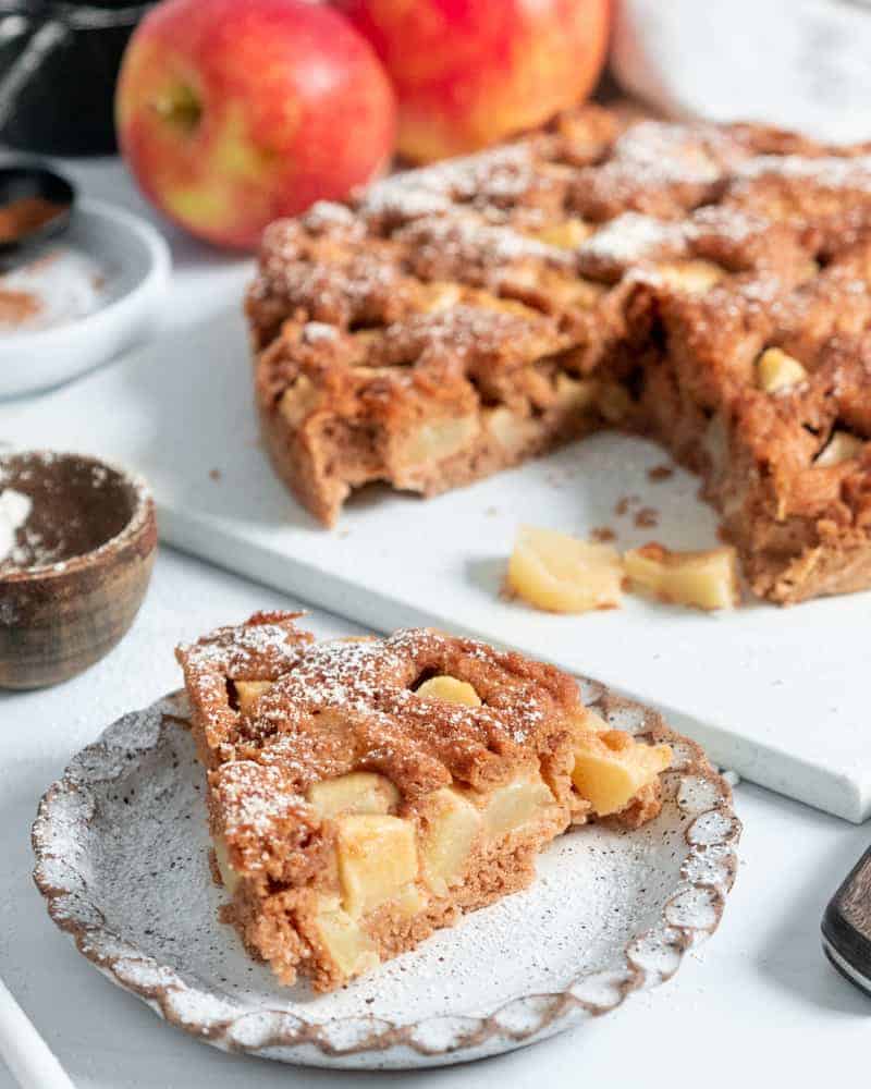 finished apple cake with two apples and measuring tools against a white background