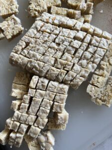 process of cutting tempeh in cubes against a white background