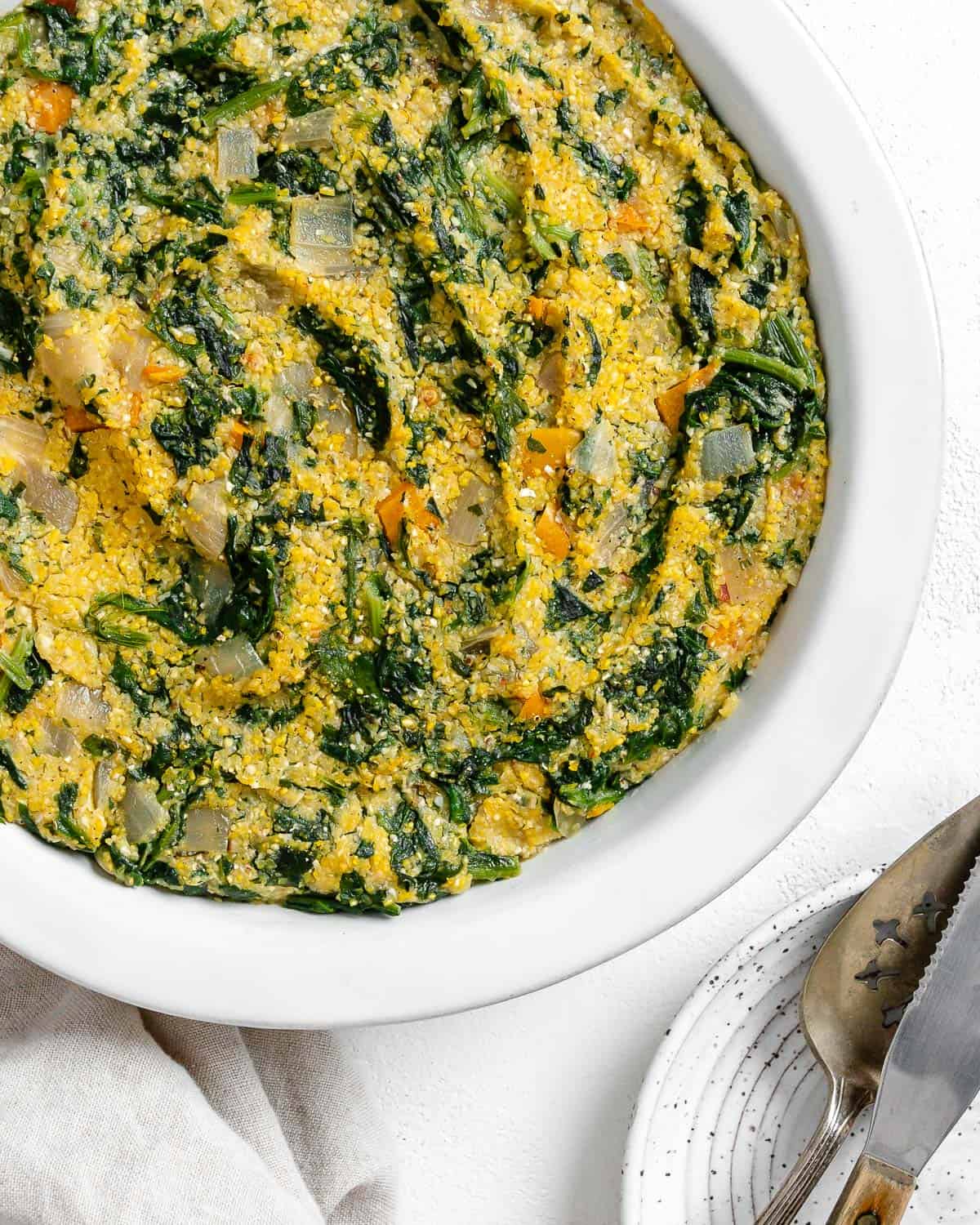 completed Garlicky Spinach and Pepper Polenta Pie in a white backing dish against a white surface