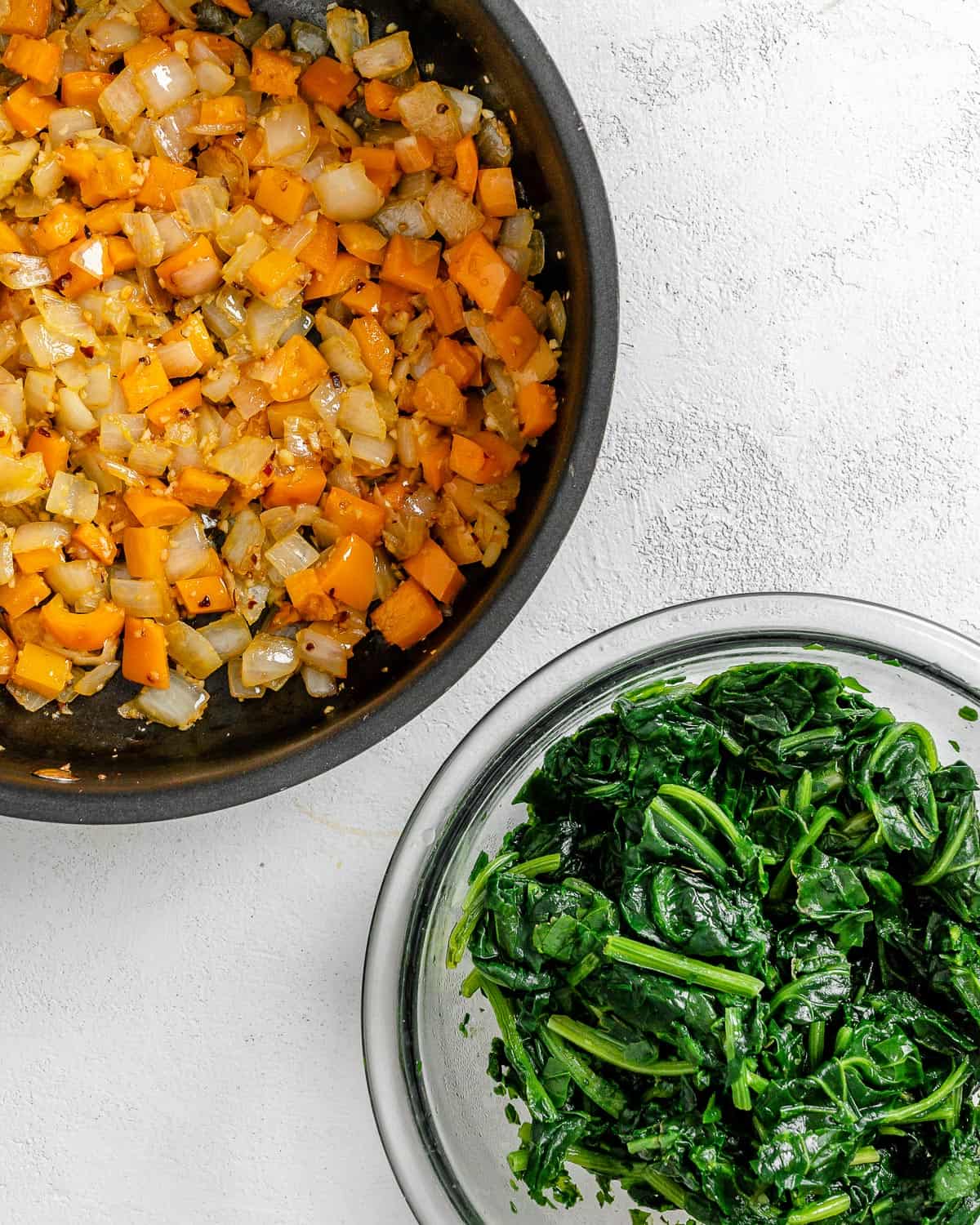 veggies in a pot alongside a bowl of spinach against a white background