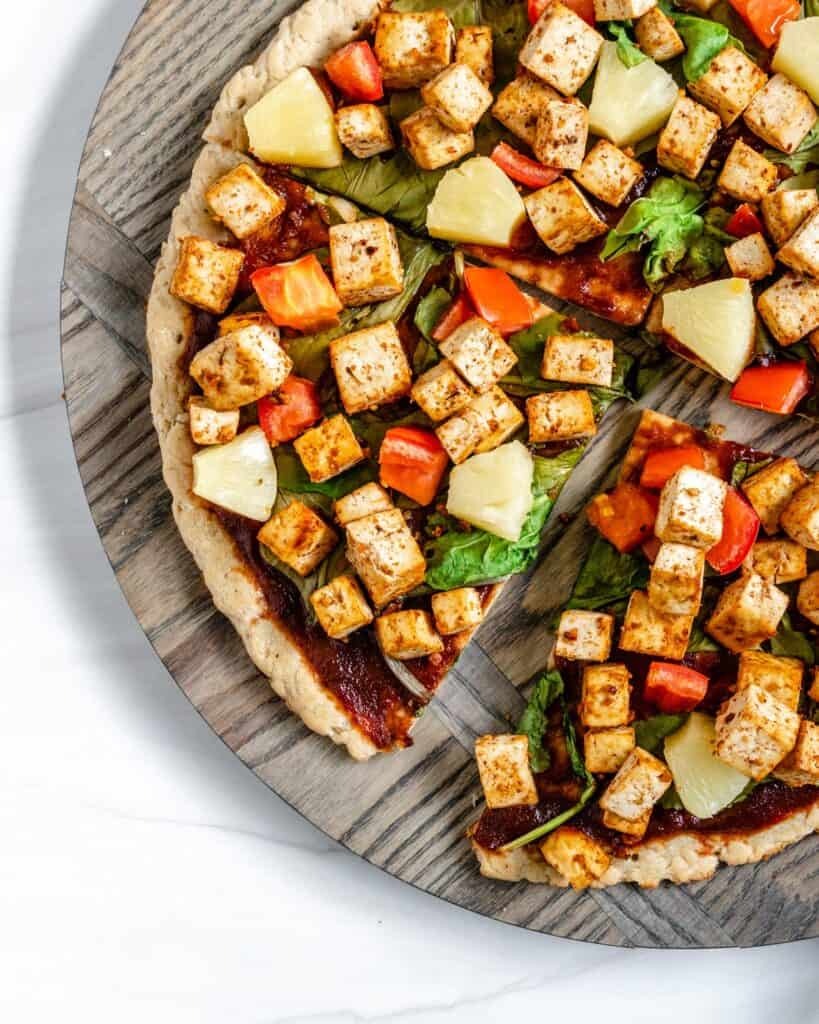 completed vegan bbq pizza sliced into quarters on a textured circular board against a white background