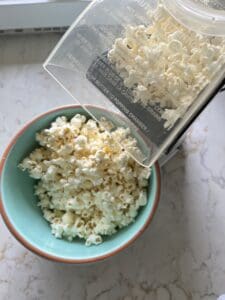 process of pouring freshly popped popcorn into blue bowl