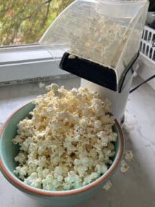 process of pouring freshly popped popcorn into blue bowl