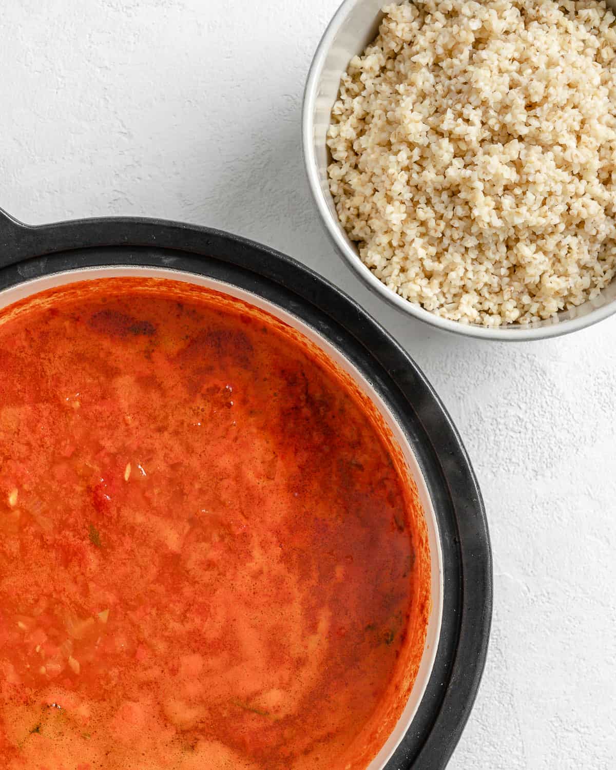 process shot of a bowl of bulgar along side Turkish Tomato, Bulgur, and Red Pepper Soup in pan