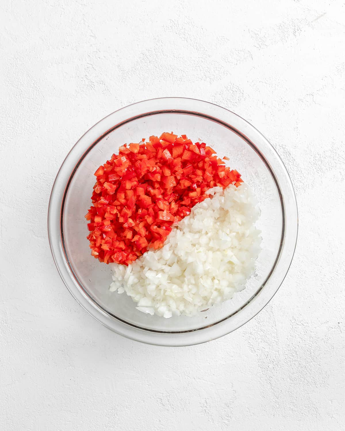 red pepper and onion minced in a glass bowl against a white surface