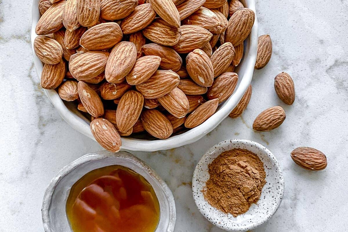 ingredients for cinnamon almonds measured out in individual bowls against white marble surface
