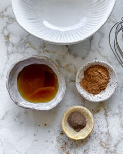 ingredients for cinnamon almonds measured out in individual bowls against white marble surface